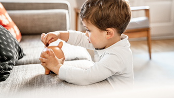 Kleiner Junge spielt mit Sparschwein im Wohnzimmer