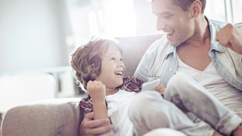 Papa mit Sohn lachend auf der Couch 