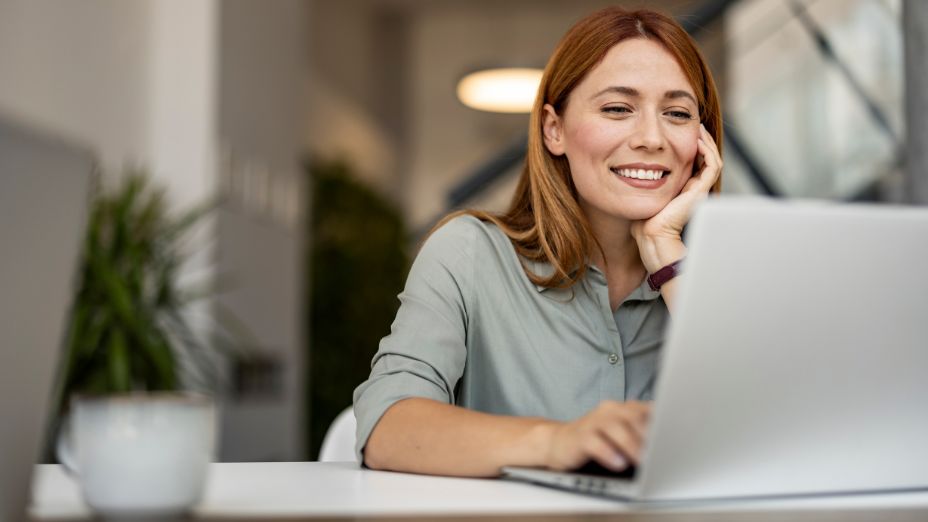 Frau sitzt am Laptop. Mit der linken Hand stützt sie ihren Kopf und mit der rechten Hand schreibt sie auf der Tastatur.