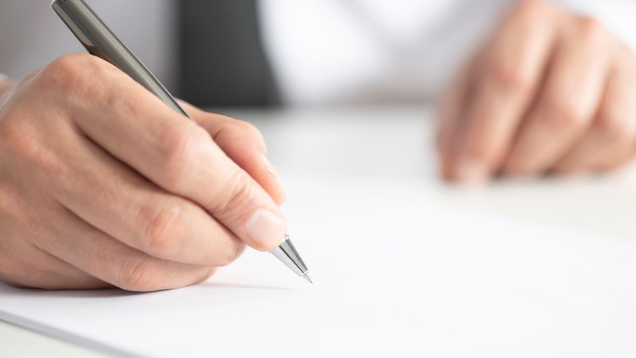 Zwei Hände sind abgebildet. Die rechte Hand hält einen Kugelschreiber und schreibt auf einem Blatt.