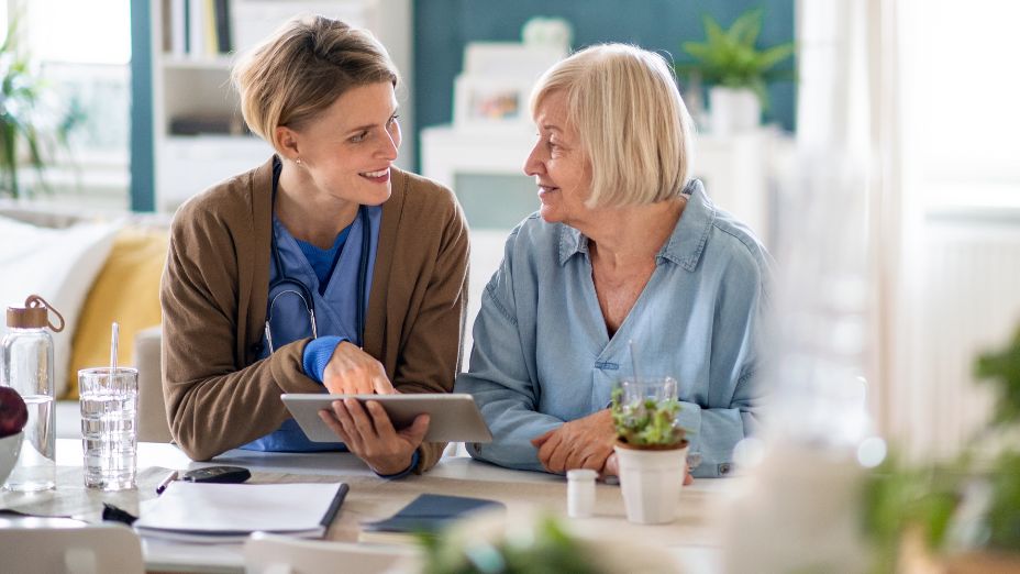 Eine Frau in blauer Pflegekleidung und eine ältere Dame stehen nebeneinander in der Küche.