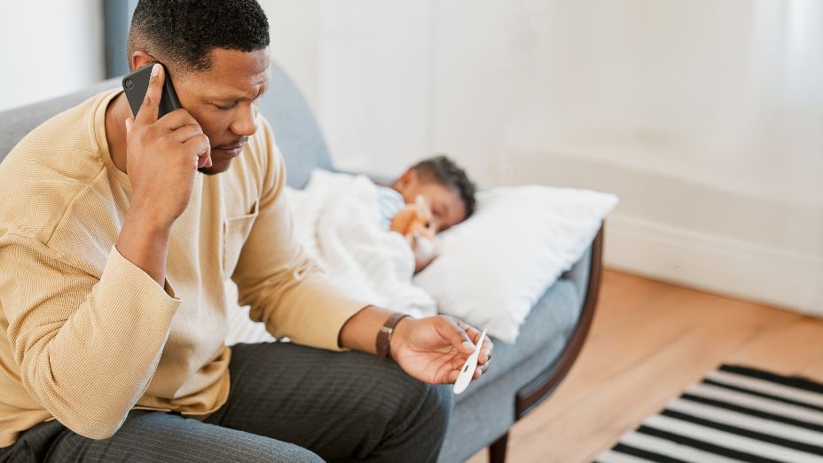 Ein Kind liegt auf einem Sofa und ich zugedeckt. Davor sitzt ein Mann und telefoniert.