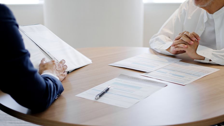 Zwei Menschen sitzen an einem Tisch. Es liegen Papiere auf dem Tisch.