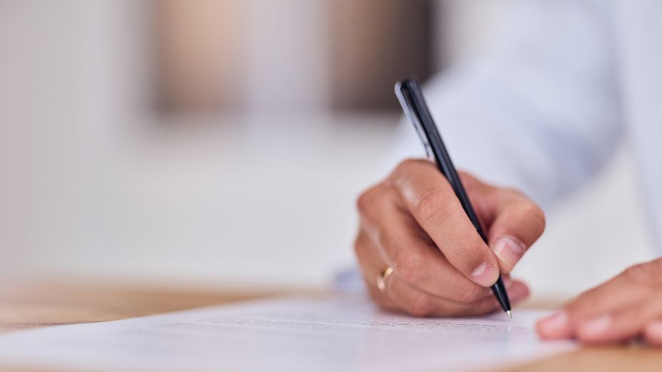 Eine Person hat einen Stift in der Hand und schreibt auf einem Blatt