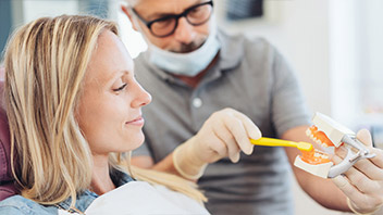 Blonde Frau bei Zahnvorsorge schaut sich Putztechnik an einem Gebiss an